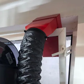 Roter 3D-gedruckter Abluftadapter mit schwarzem Schlauch in einem gekippten Fenster